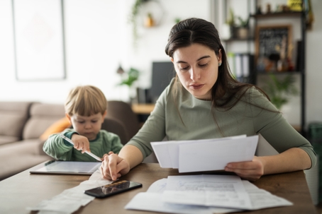 mother calculating expenses with child playing in the background