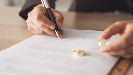 person signing divorce papers while holding wedding ring